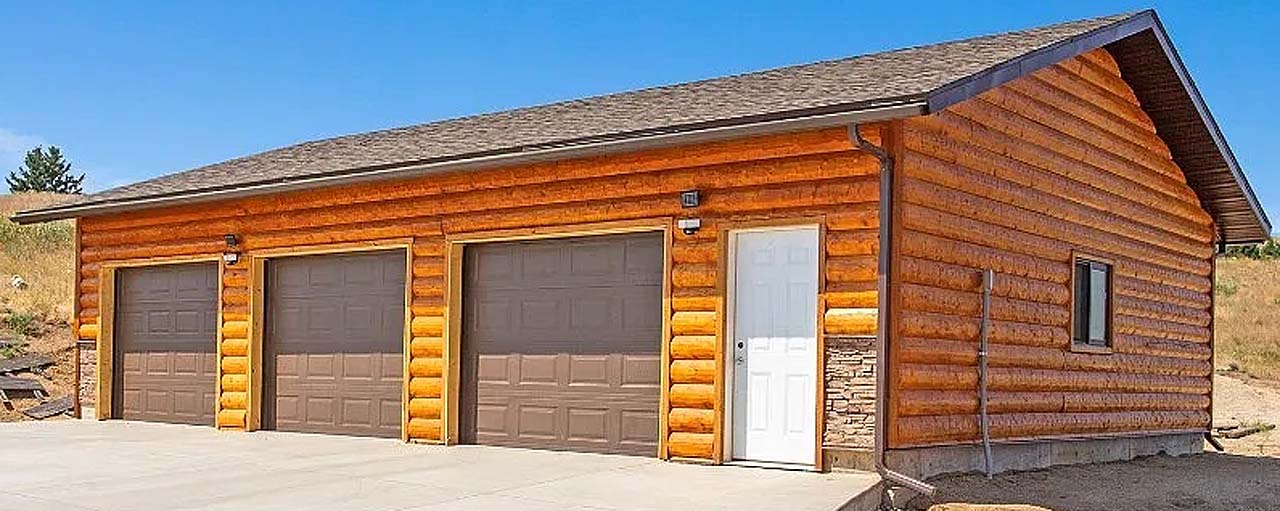 A wooden garage with three brown doors and a white door on the side, set against a clear blue sky.