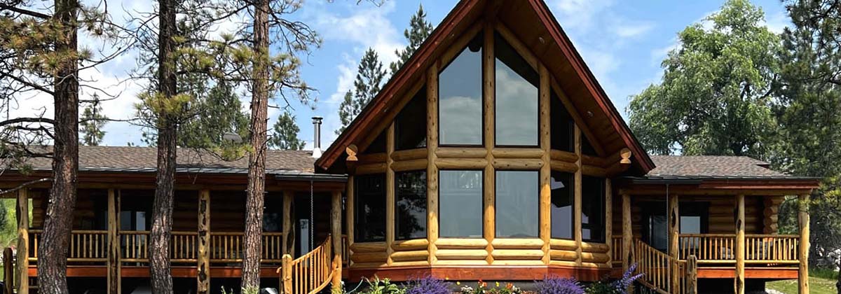 Beautiful log cabin surrounded by tall trees, featuring large windows and a welcoming porch, perfect for nature lovers.