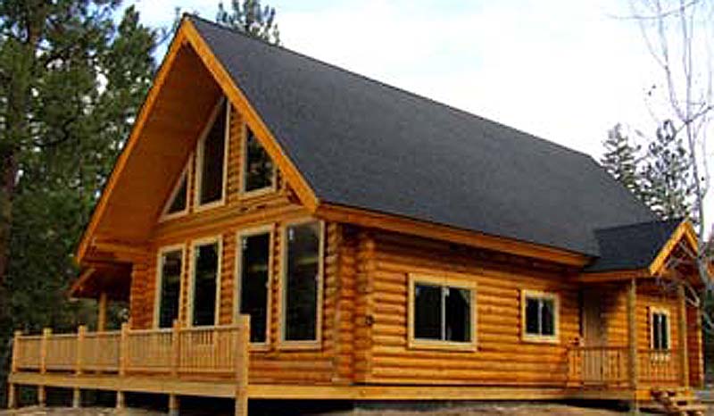 A large log cabin with a sloped roof, featuring multiple windows and a front porch surrounded by trees.