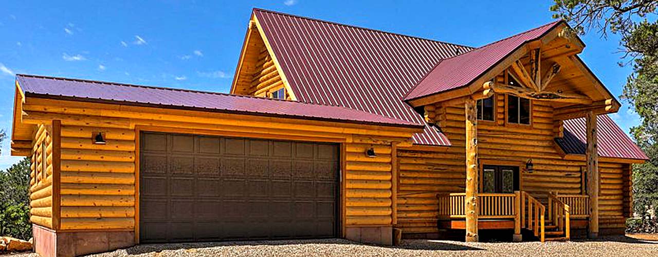 A log cabin house with a metal roof, large garage door, and porch in a natural setting.