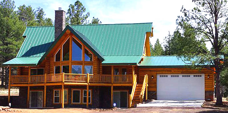 A large log cabin-style house with a green metal roof, featuring multiple balconies and large windows, surrounded by trees.
