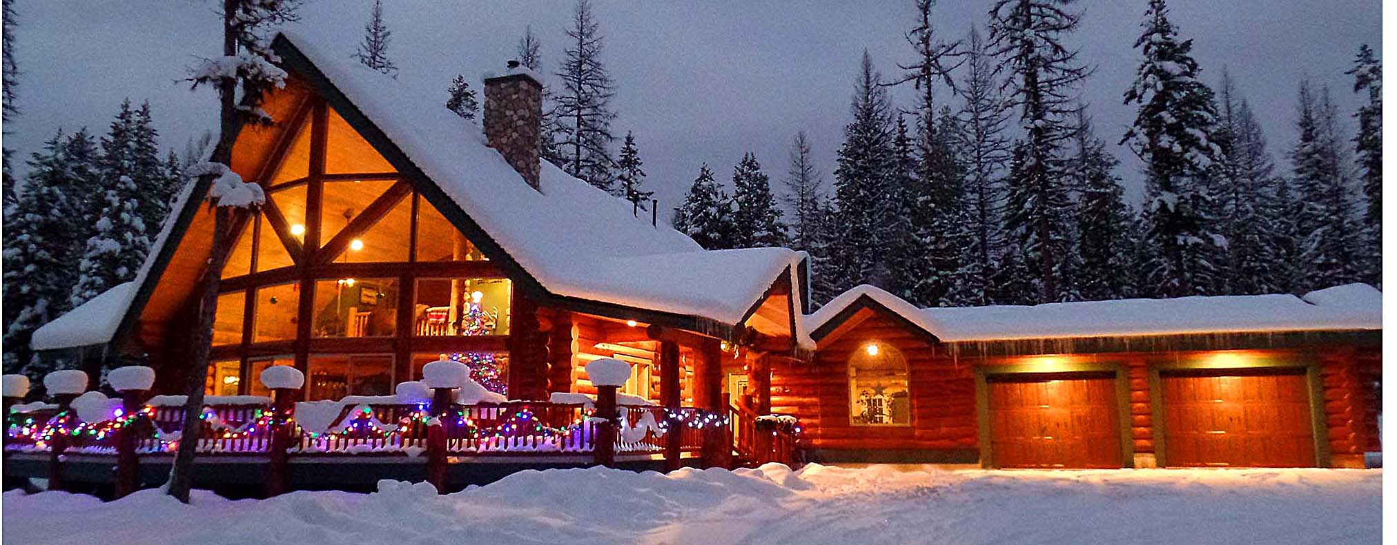 A cozy log cabin covered in snow with warm lights glowing from the windows, surrounded by tall trees.