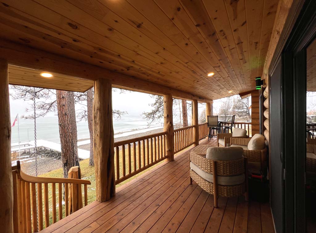 A wooden porch overlooking a body of water with seating and a view of trees.