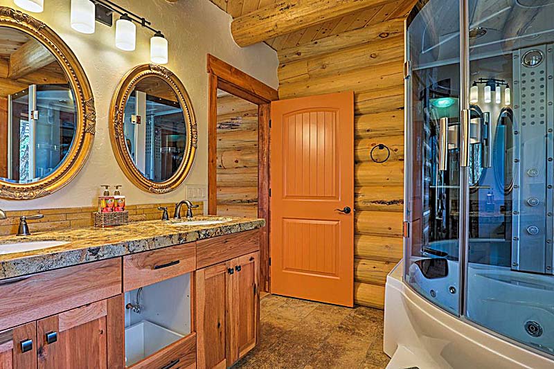 A luxurious log home bathroom featuring wooden log walls, a double sink with ornate mirrors above, an orange door, and a modern shower enclosure with additional features.