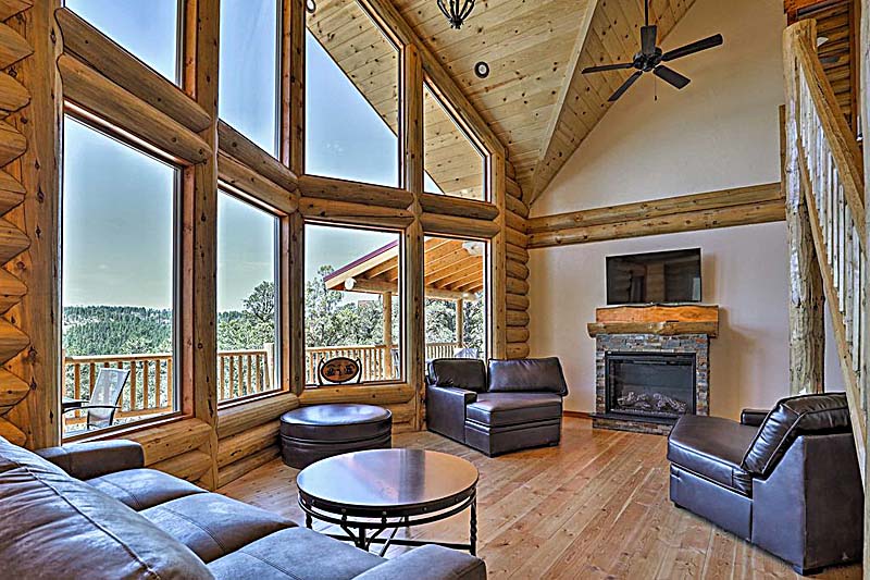 A spacious log home living room with large windows, a fireplace, and modern furniture.