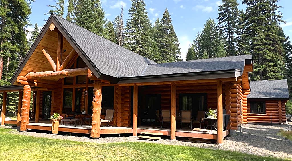 A log cabin with a modern design surrounded by tall trees and green grass.