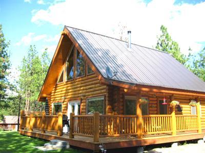 A log cabin with a triangular roof, large windows, and a wooden deck surrounded by trees.