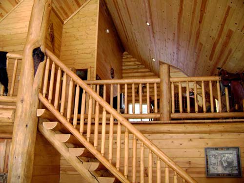 Warm log home interior with rustic wooden stairs and railings, showcasing craftsmanship and cozy ambiance.