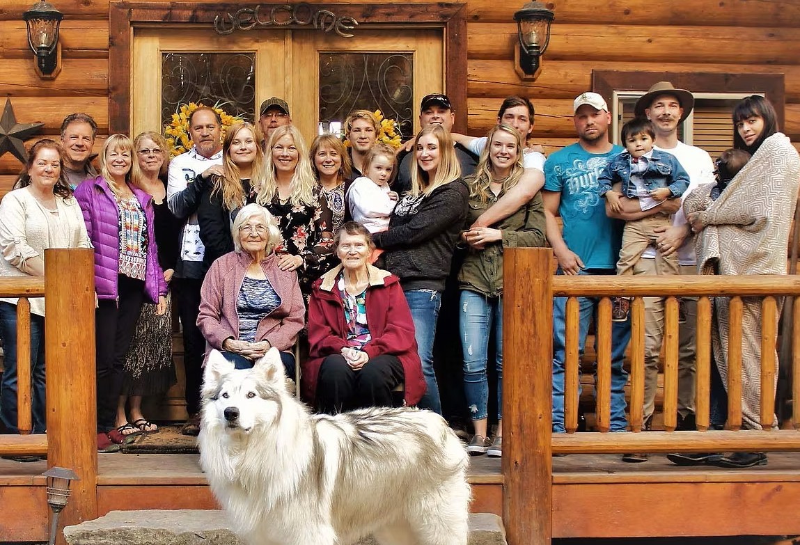 The Lazarus family gathering on a wooden porch with a friendly dog in front, showcasing love and togetherness in a cozy setting.