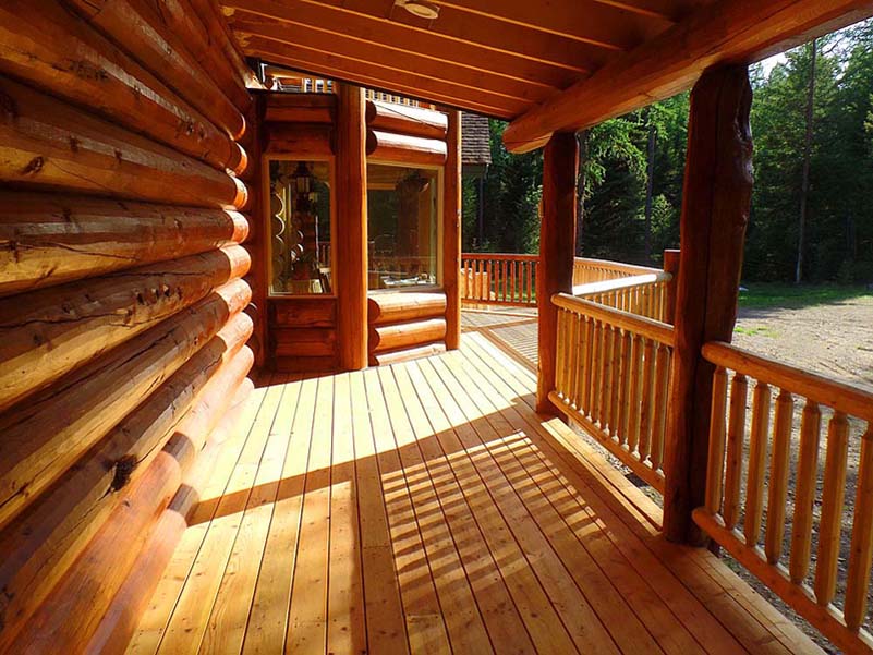 A wooden deck of a log cabin, featuring a railing and surrounded by trees.