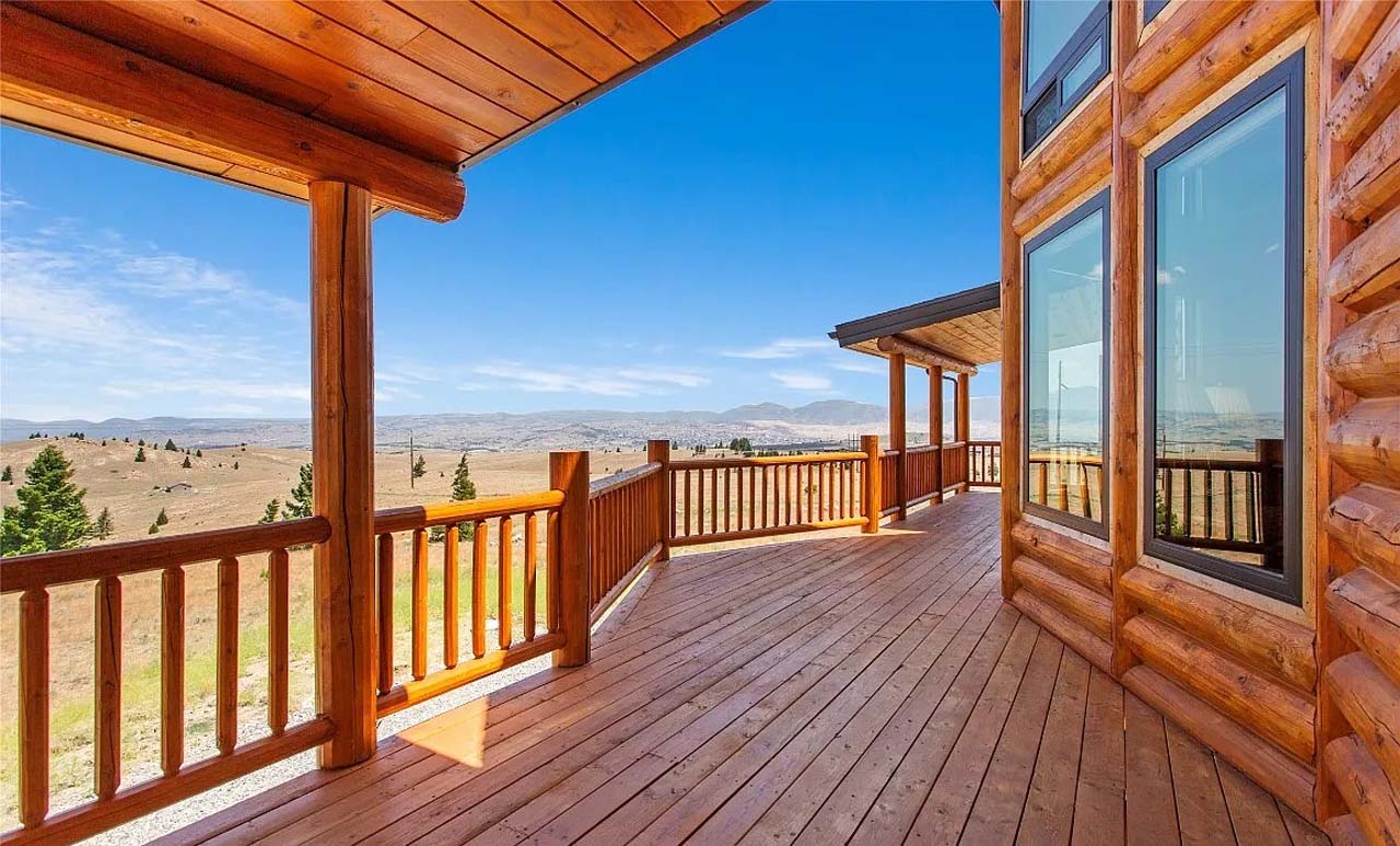 A wooden porch with a view of rolling hills and blue sky, featuring log cabin architecture.