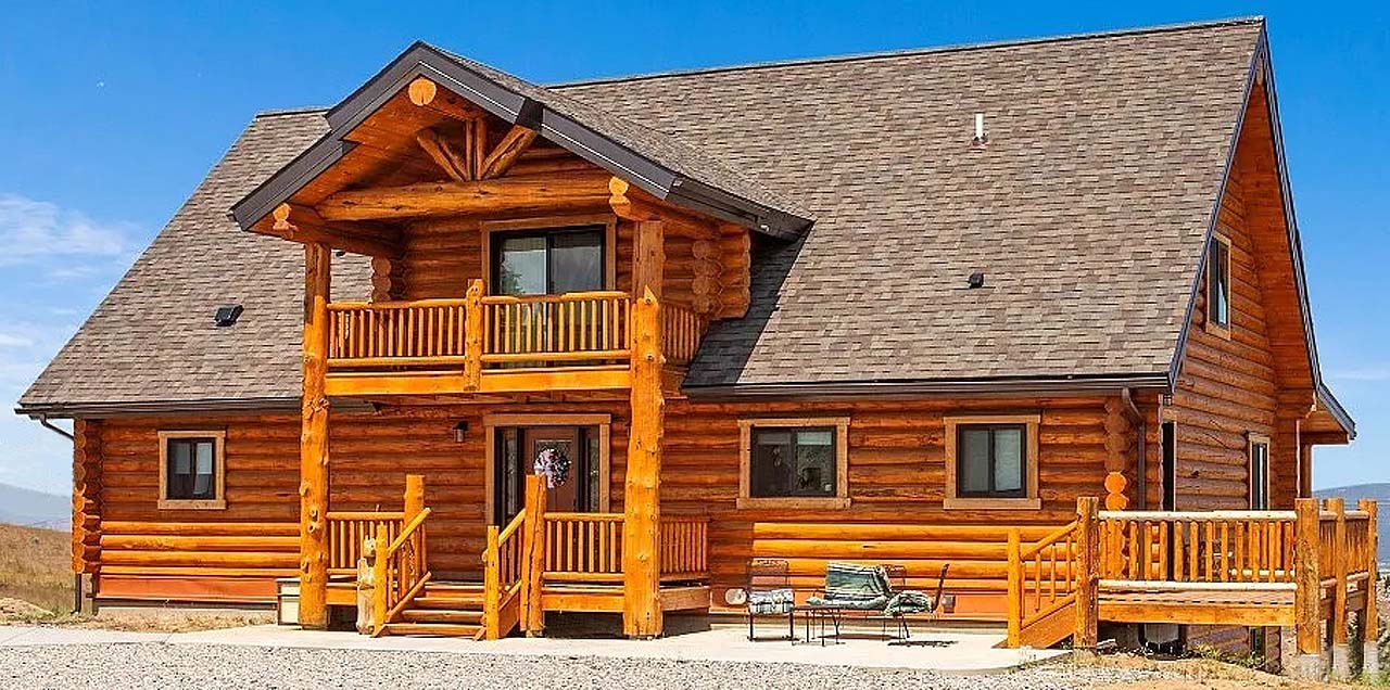 A log cabin-style house with a steep roof, wooden balconies, and large windows, set against a clear blue sky.