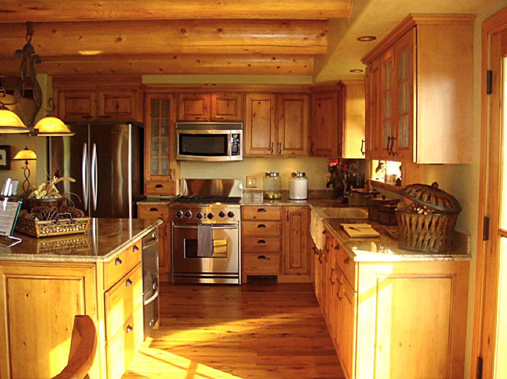 A modern log home kitchen with wooden cabinetry, stainless steel appliances, and a spacious layout featuring a granite countertop and wooden floors.