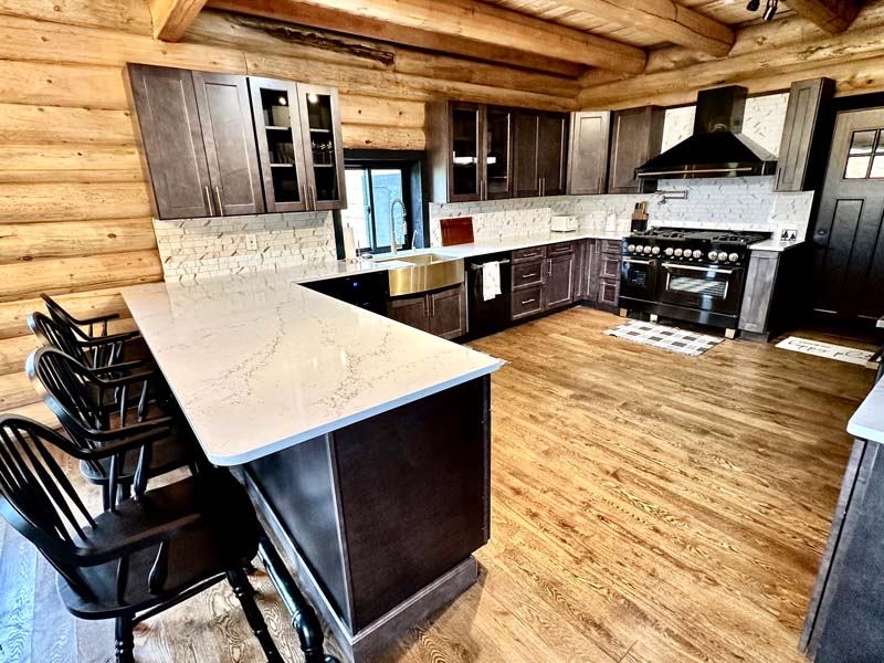 A spacious log home kitchen featuring wooden log walls, a large island with bar stools, modern appliances, and ample cabinet space.
