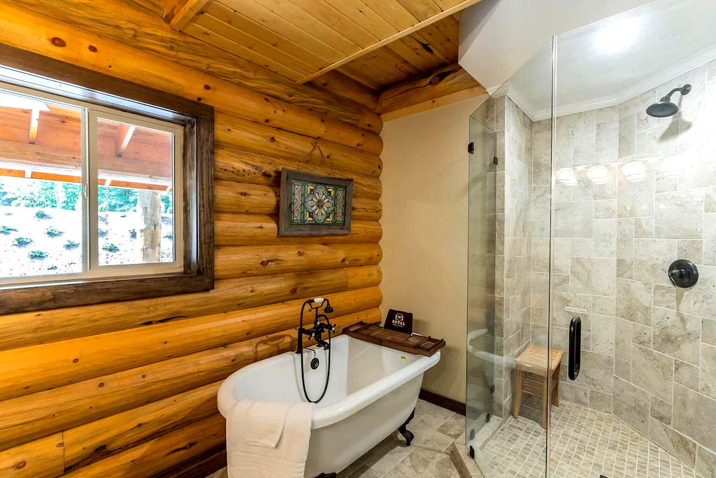 A log home bathroom featuring a glass shower, a vintage-style freestanding tub, and wooden log walls.