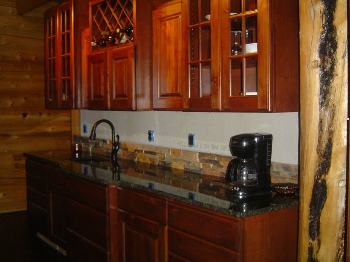 A log home kitchen area featuring wooden cabinets, a granite countertop, a coffee maker, and wine storage.