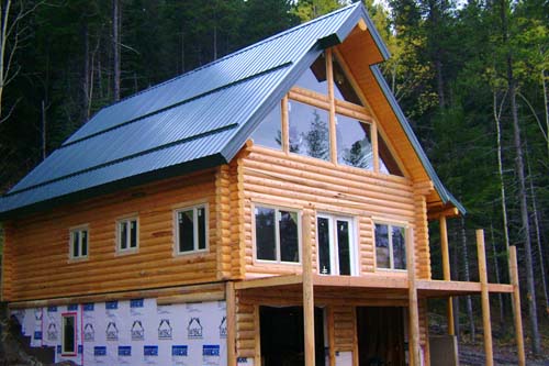 A large log home cabin with a triangular roof and multiple large windows, surrounded by trees.