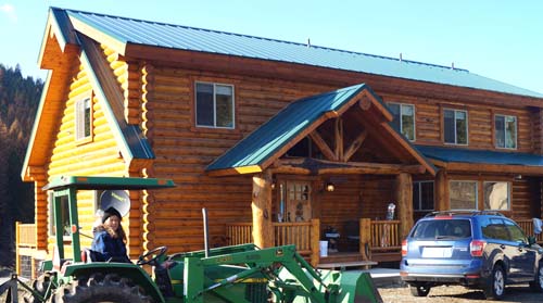 Person driving tractor in front of a wooden cabin house