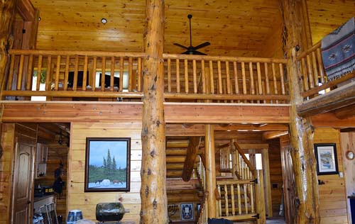 Rustic cabin interior with wooden beams and staircase.