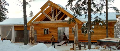 Log cabin in a snowy forest setting with blue sky overhead