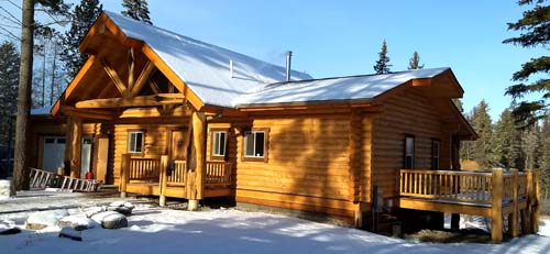 Log cabin in a snowy forest setting with blue sky overhead
