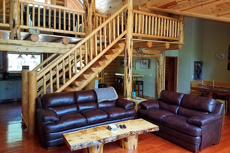 Rustic cabin living room with wooden staircase and sofas