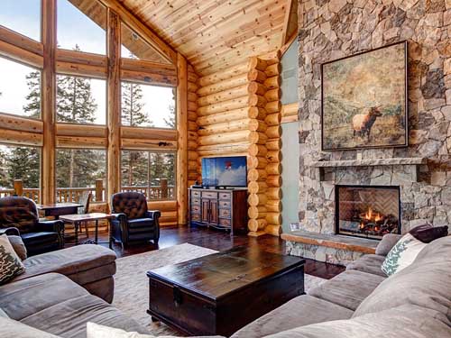 Cozy log cabin living room with large windows and fireplace.
