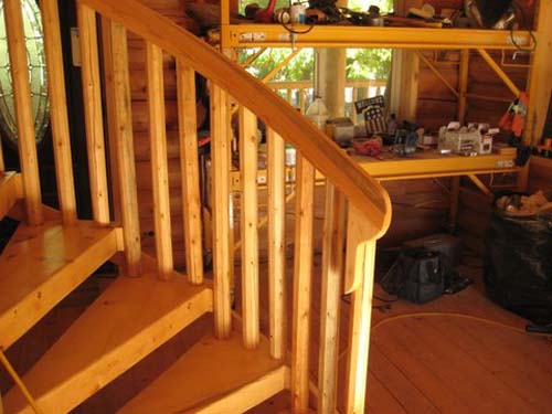 Wooden spiral staircase next to workshop shelves and tools.